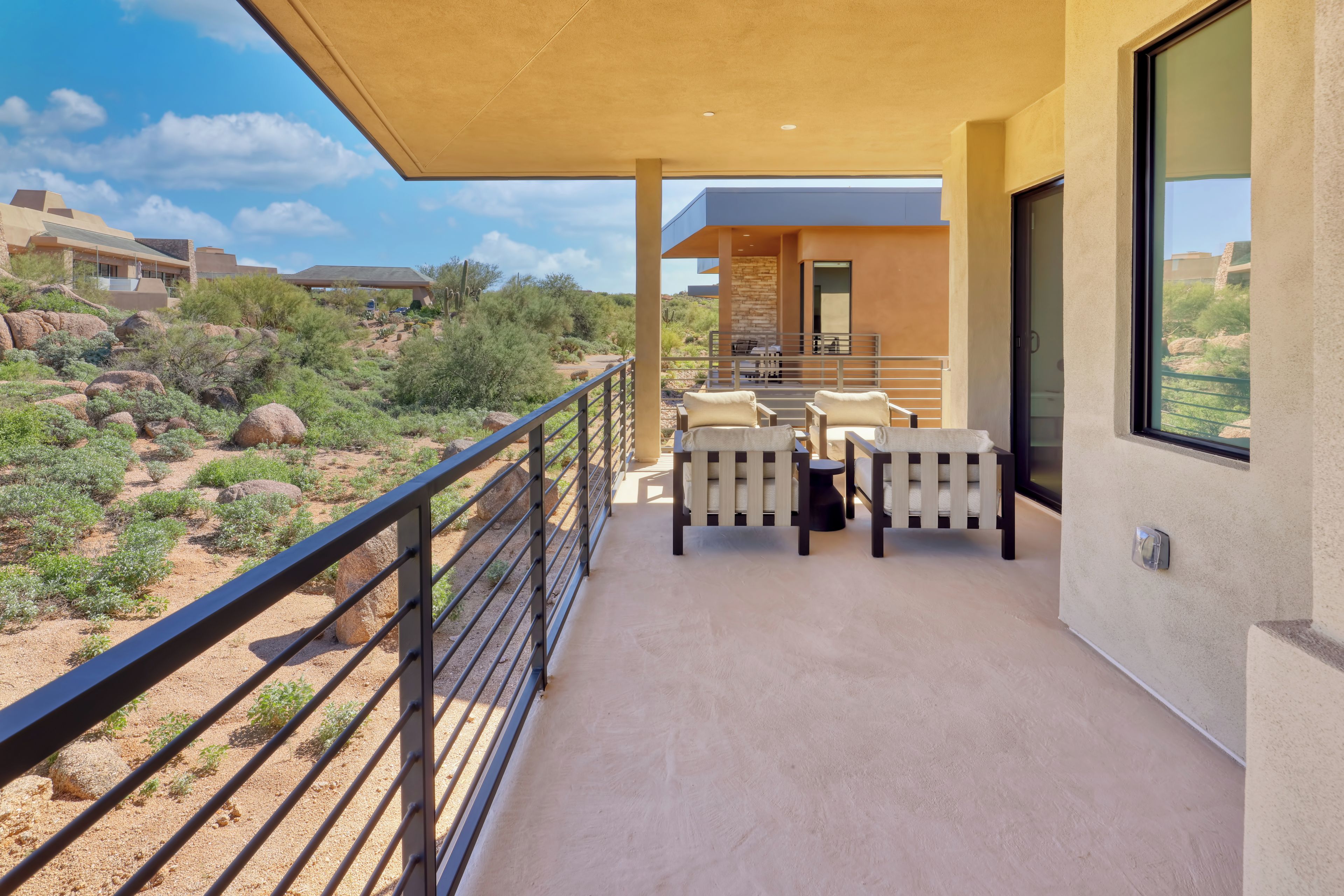 A balcony with a view of a desert landscape, a table with chairs, and a modern building in the background.