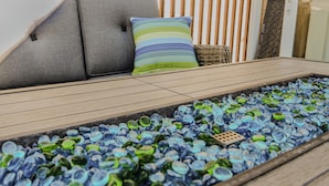 Ein sonnendurchfluteter Außenbereich mit Holzterrasse, gepolsterten Sitzgelegenheiten und einem wasserführenden Mosaikbrunnen.
