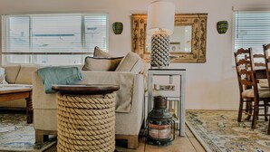 Ein Wohnzimmer mit einer Couch, einem runden Holztisch, einer Lampe, einem Spiegel und einem gemusterten Teppich.