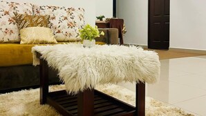 A modern living room with a sofa, a fluffy white pouf, a ceiling fan, and a dark wooden door. - Celestial Villas and Apartments (Negombo)