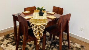 A dining area with a table set for four, surrounded by wooden chairs, a patterned tablecloth, and a small potted plant. - Celestial Villas and Apartments (Negombo)