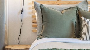Een bed met een houten hoofdbord, een groen gebreide deken en meerdere kussens.