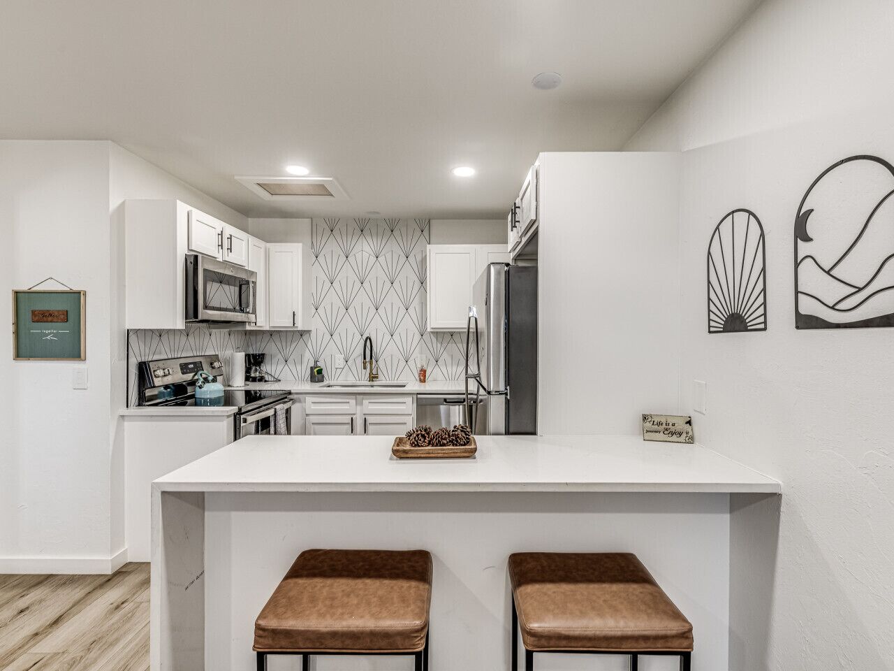 Una cocina moderna con armarios blancos, una isla central con taburetes y decoración en la pared.