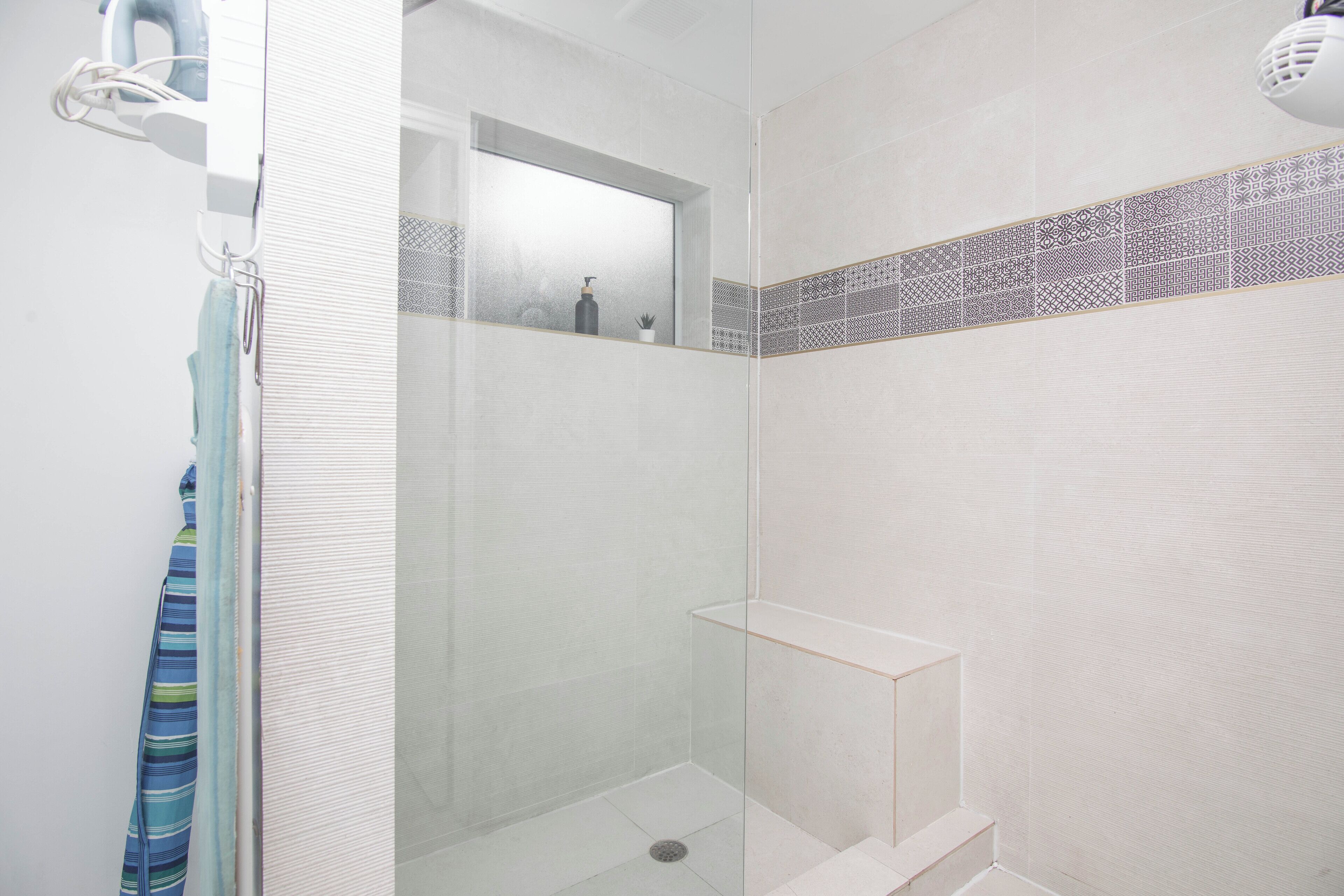 A shower with a glass door, a towel rack, and a shelf with toiletries.