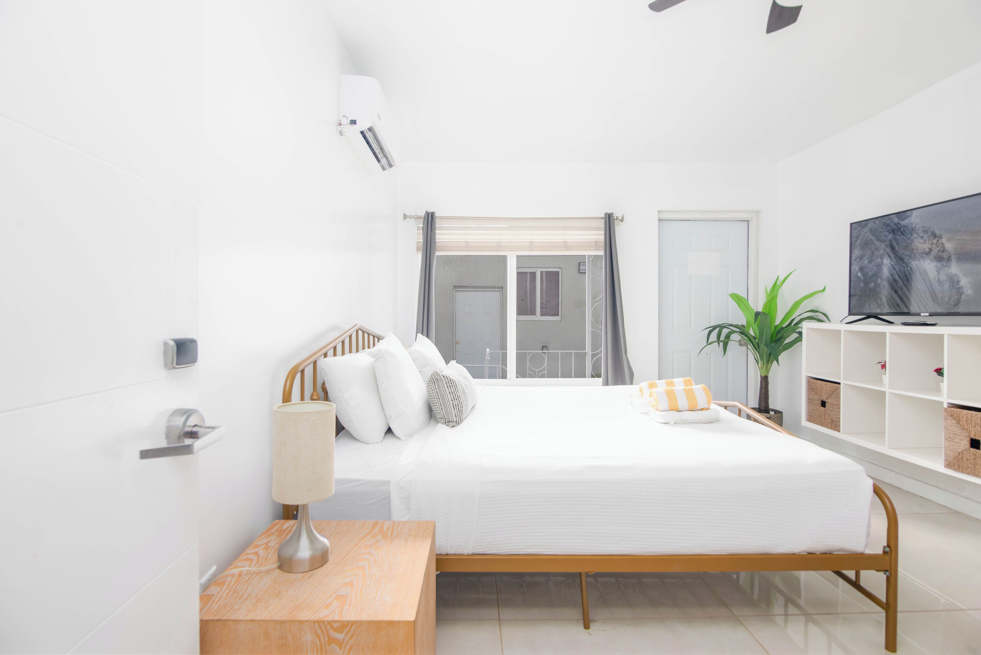 A modern bedroom with a bed, bedside table, lamp, TV, and a potted plant.