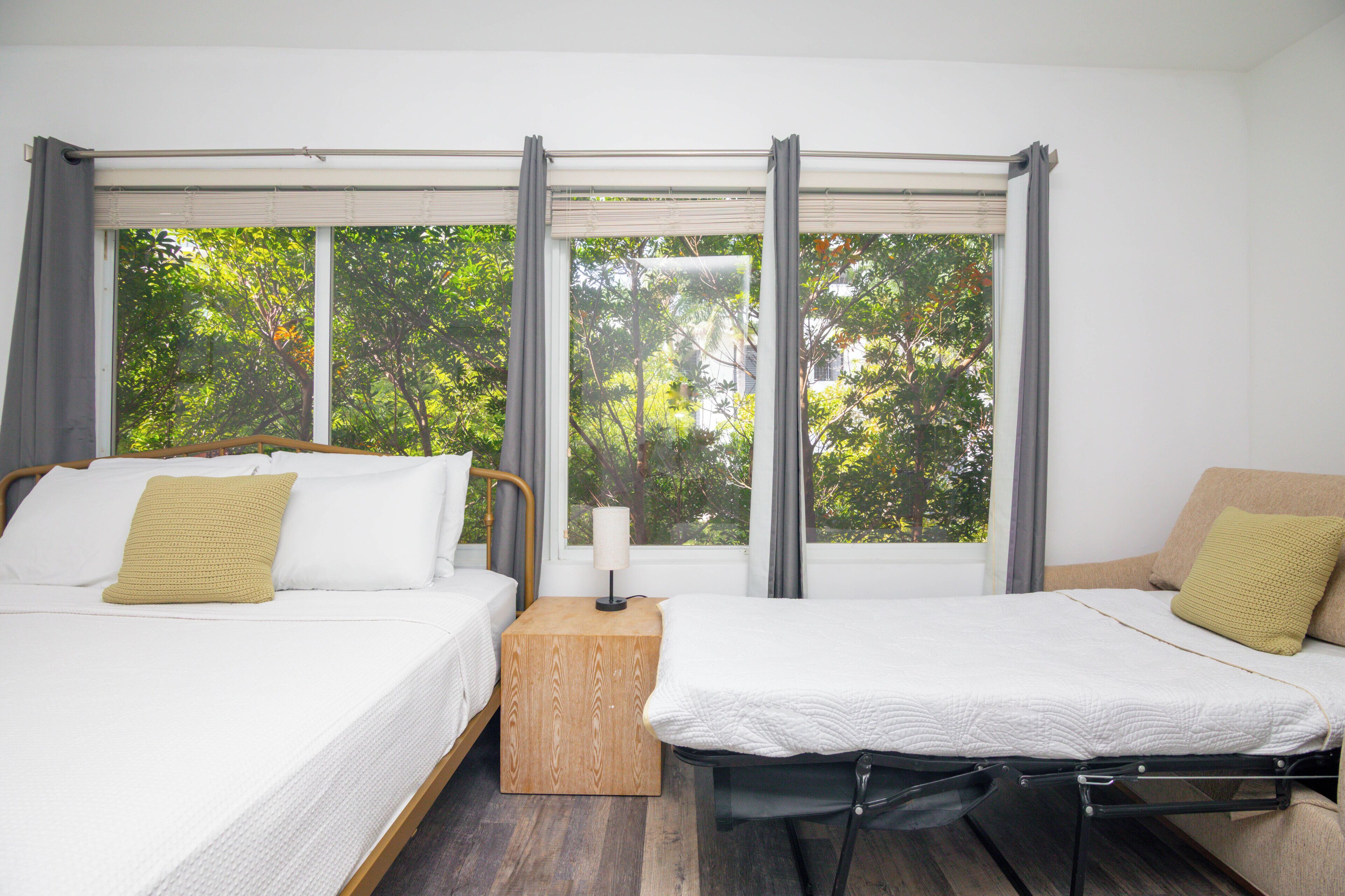 Une chambre avec deux lits, une table de chevet en bois et une fenêtre donnant sur des arbres.