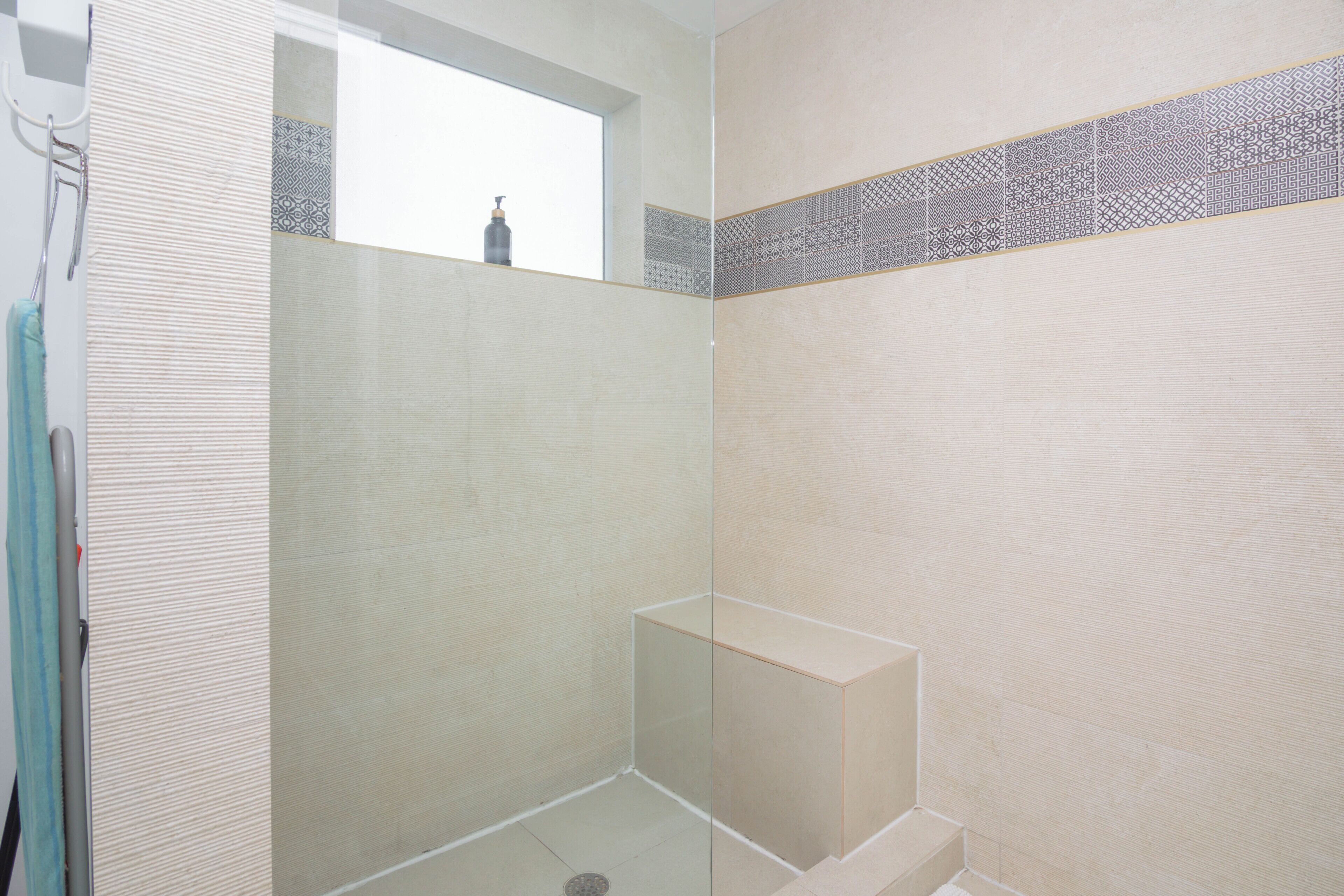 Een badkamer met een douche, een raam en een betegelde rand met een patroon.