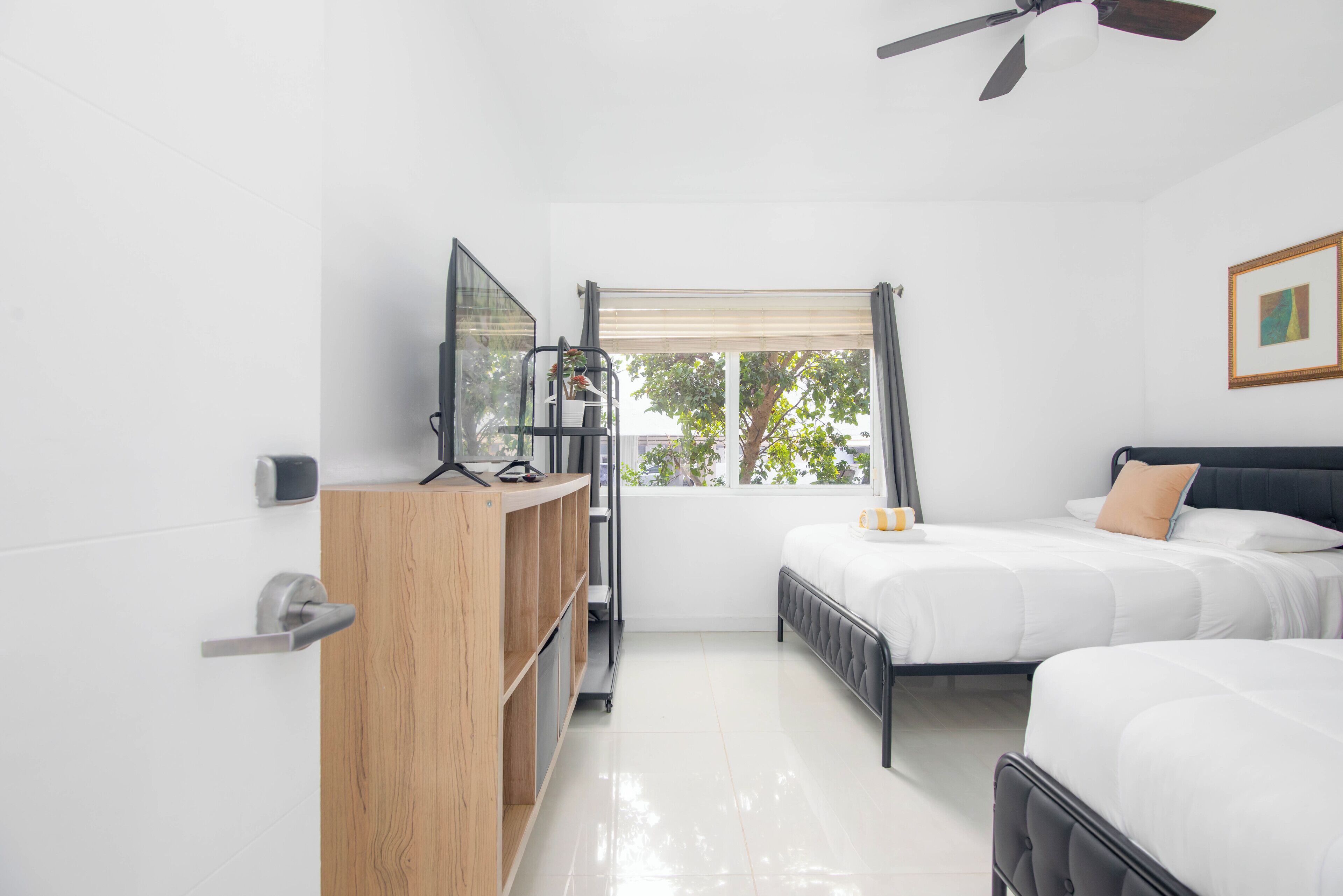 A bedroom with two beds, a wooden cabinet, a television, and a window with curtains.
