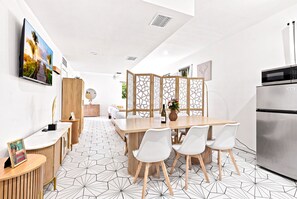 Eine moderne Küche mit Essbereich, ausgestattet mit einer großen Kochinsel, weißen Stühlen und einem Kühlschrank.
