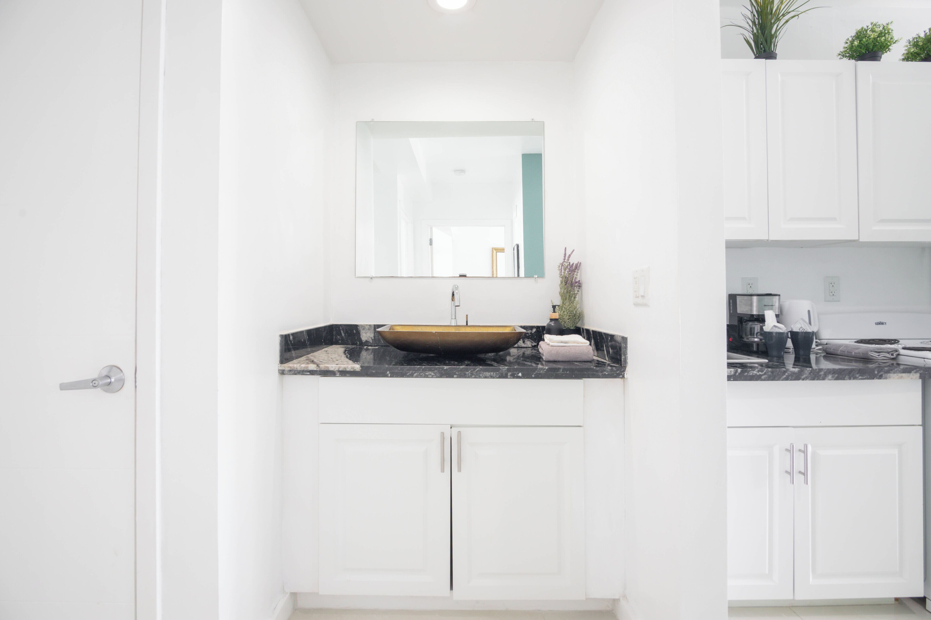 A modern bathroom with white cabinetry, a black marble countertop, and a large mirror above the sink.