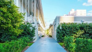 A narrow, tree-lined pathway leading to a building with a modern architectural style, featuring large windows and a balcony. - Boutique Apartments Flamingo (Miami Beach)