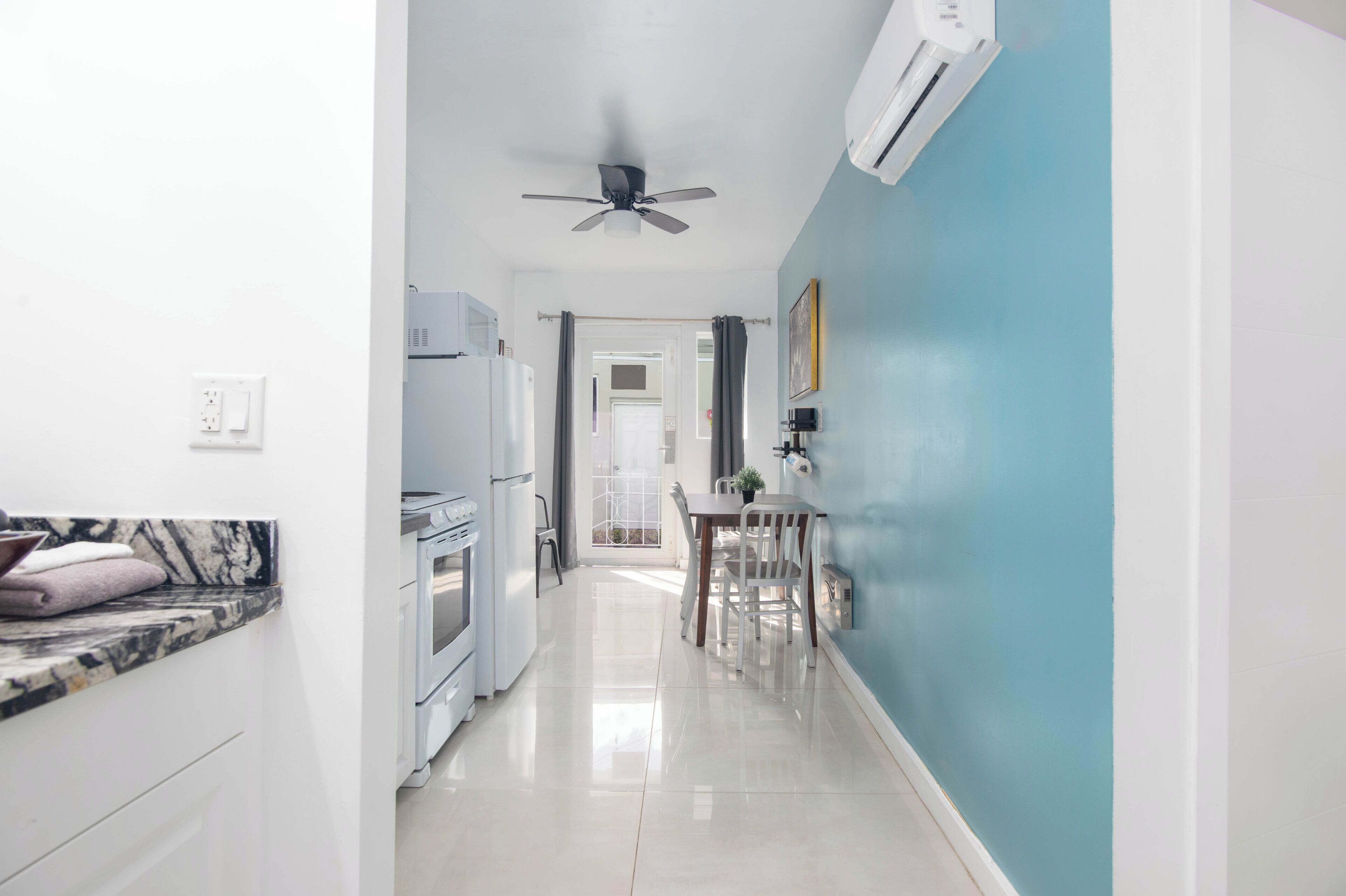 Une cuisine moderne avec des appareils électroménagers blancs, un ventilateur de plafond et un coin repas comprenant une table et des chaises.
