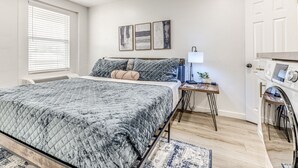 Une chambre avec un grand lit, une table de chevet avec une lampe et un lave-linge encastré.