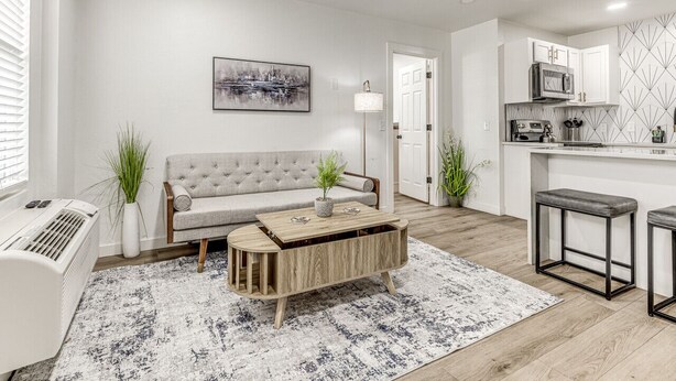 Un salon moderne comprenant un canapé, une table basse et un coin cuisine équipé d’un four à micro-ondes et de placards.