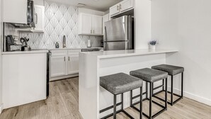 Une cuisine moderne avec des meubles blancs, un réfrigérateur en acier inoxydable et un coin bar équipé de tabourets.