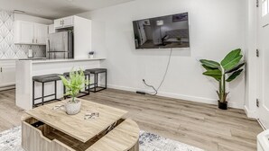 Une cuisine moderne avec des meubles blancs, un réfrigérateur encastré et un coin repas comprenant une table et des chaises en bois.
