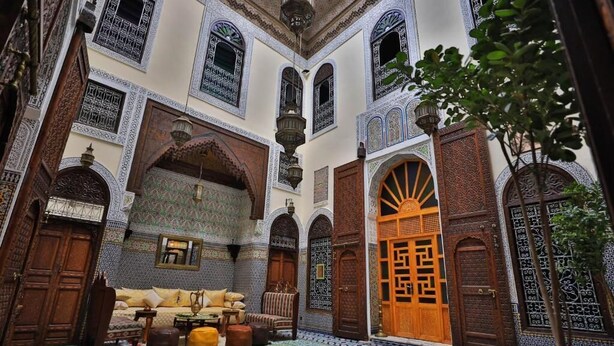 A traditional Moroccan interior with ornate arches, a patterned tile floor, and a wooden door. - Riad SOULTANA every stay tells a story (Fes)