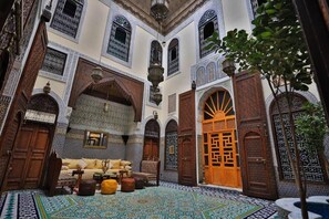 Un interior marroquí tradicional con arcos ornamentales, un suelo de baldosas estampadas y una puerta de madera.