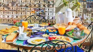A table set with breakfast items including croissants, bread, and fruit, with a scenic view in the background. - Riad SOULTANA every stay tells a story (Fes)