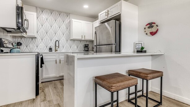A modern kitchen with white cabinetry, stainless steel appliances, and a central island with stools. - Remodeled Modern 1 Bed (Oklahoma City)