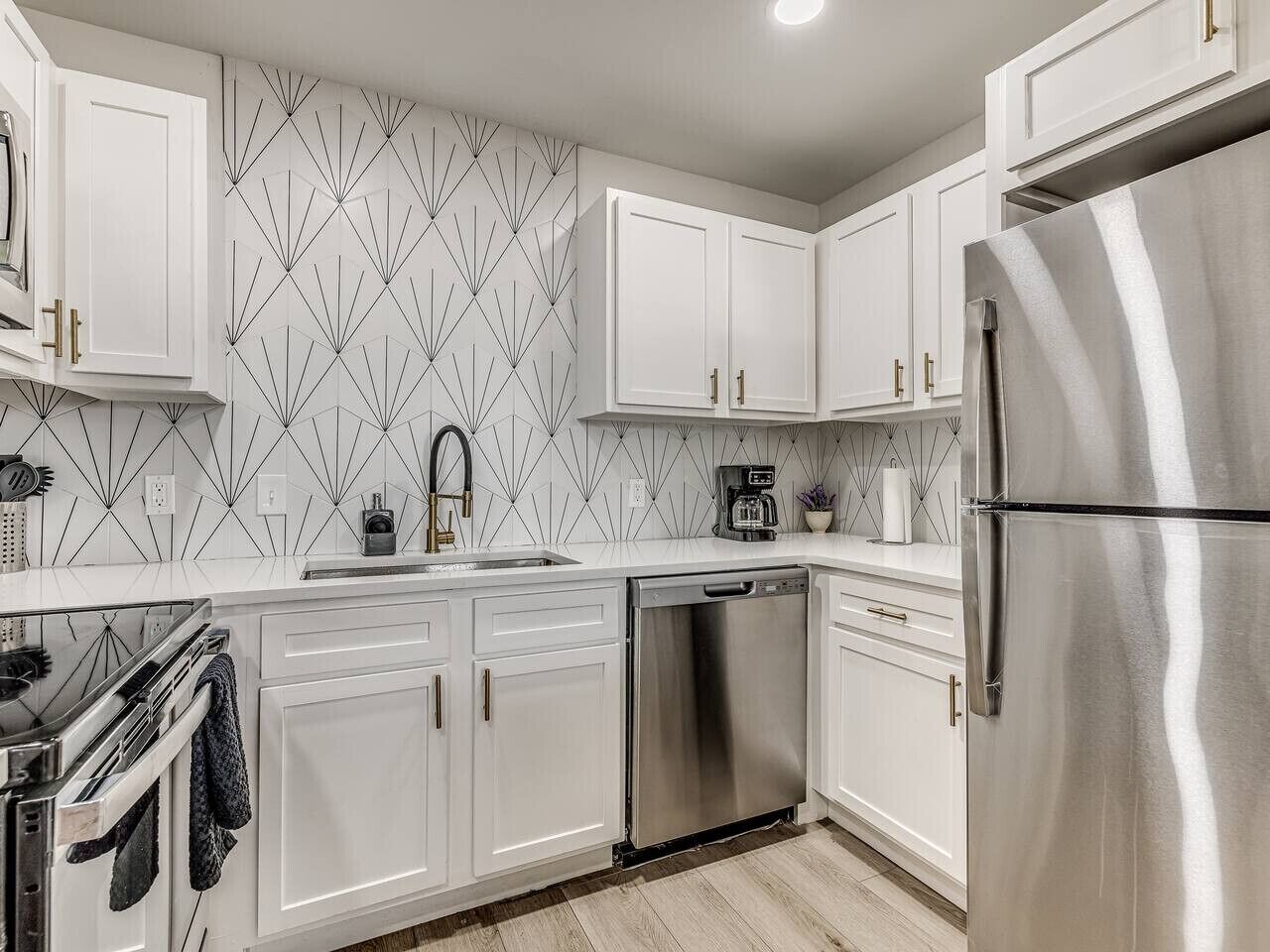 A modern kitchen with white cabinets, stainless steel appliances, and a geometric backsplash.