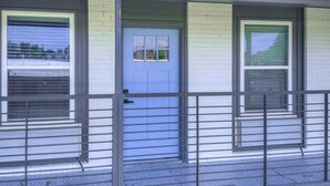 A building with a blue door, two windows with shutters, and a metal railing in front. - Remodeled Modern 1 Bed (Oklahoma City)