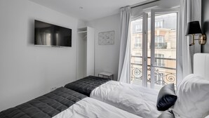 A modern hotel room with a bed, a TV, a window with a view of buildings, and a small table. - Double-bed or twins Studio in Apart'hotel Le Bellevue (Paris)