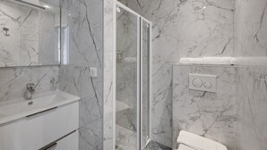 A modern bathroom with a marble wall, a glass shower enclosure, a white sink, and a toilet. - Double-bed or twins Studio in Apart'hotel Le Bellevue (Paris)