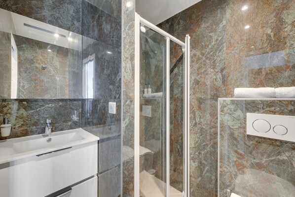 A modern bathroom with a marble sink, glass shower enclosure, and a towel rack.