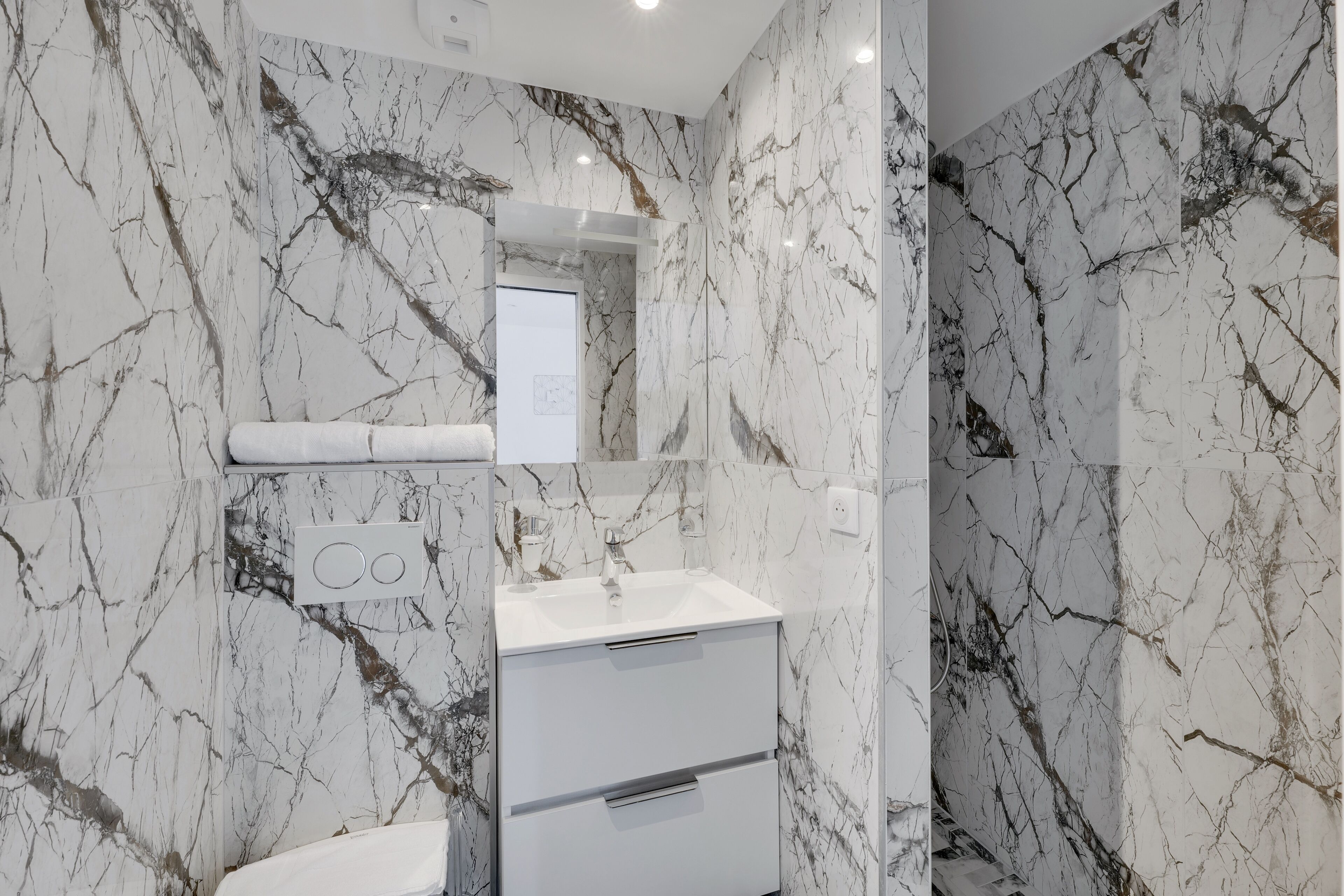 A bathroom with marble walls, a white sink, and a mirror.