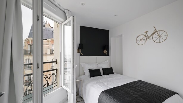 Un dormitorio con cama, cabecera negra, decoración de bicicleta en la pared y vista a un balcón con barandilla.