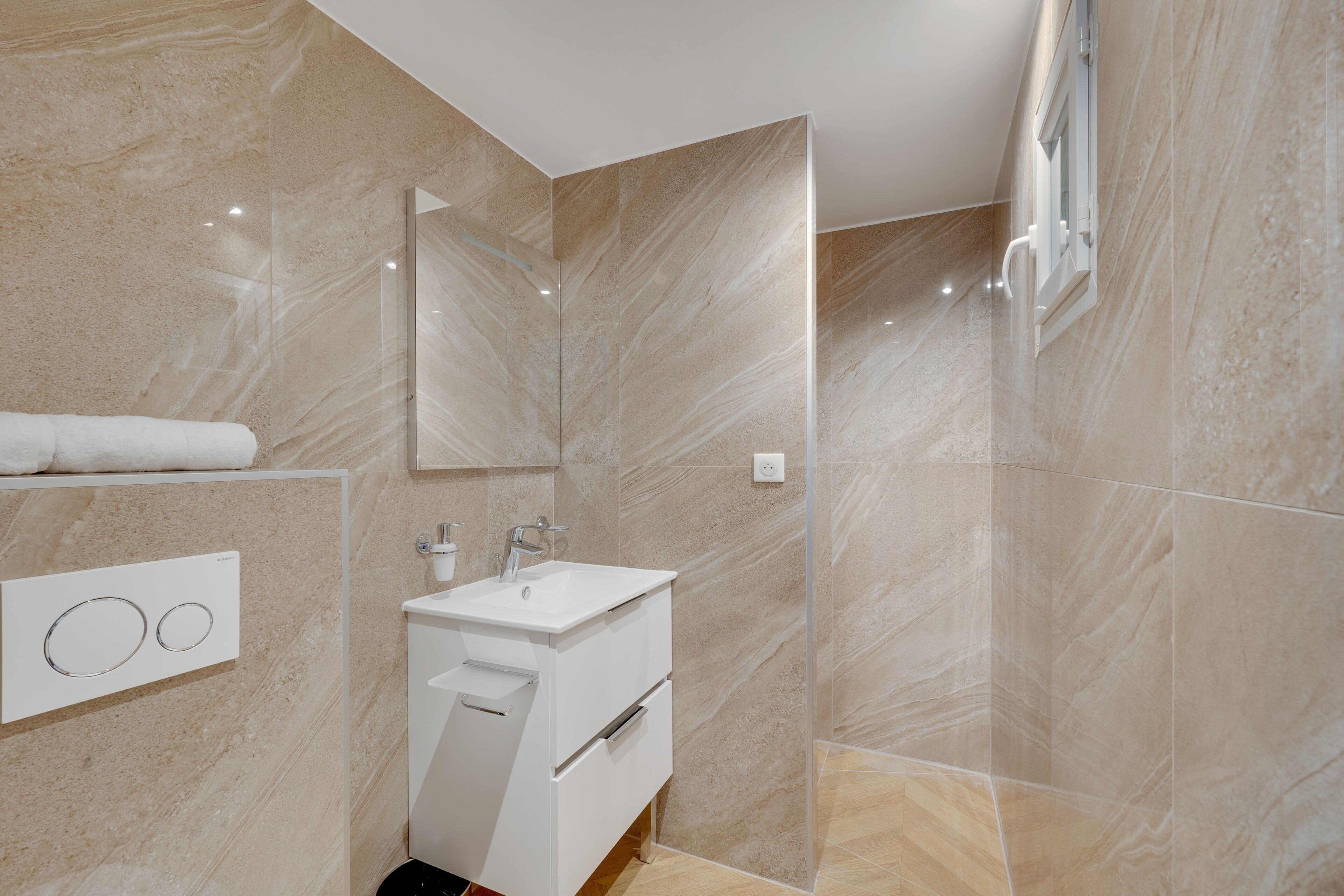 A modern bathroom with a marble wall, a white sink, and a glass shower enclosure.