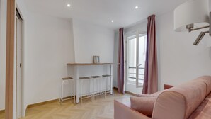 Una sala de estar moderna con un sofá, una zona de bar con taburetes y un ventanal con cortinas.