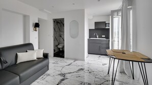 Una sala de estar moderna con un sofá de cuero negro, una mesa de centro tejida y un suelo de mármol.