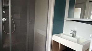Une salle de bain moderne avec une douche à l’italienne en verre, un lavabo blanc et un miroir au-dessus.