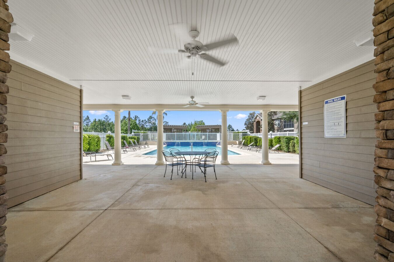 Un área de piscina cubierta con mesa y sillas, ventilador de techo y vistas a la piscina.