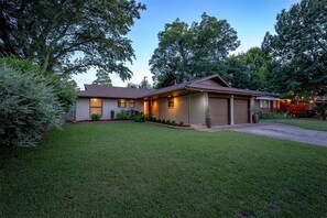 A single-story house with a garage, a well-maintained lawn, and mature trees in the background.