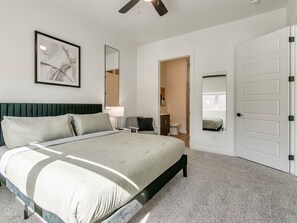 Een slaapkamer met een bed, een plafondventilator, een deur en een spiegel.