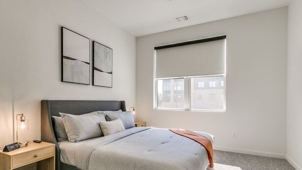 Une chambre à coucher avec un lit, des tables de chevet, une fenêtre et des œuvres d’art accrochées au mur.