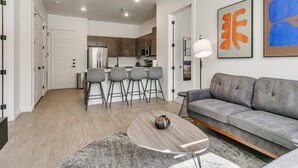 Un salon moderne avec un canapé gris, une table basse et un coin repas comprenant des chaises, et une cuisine en arrière-plan.