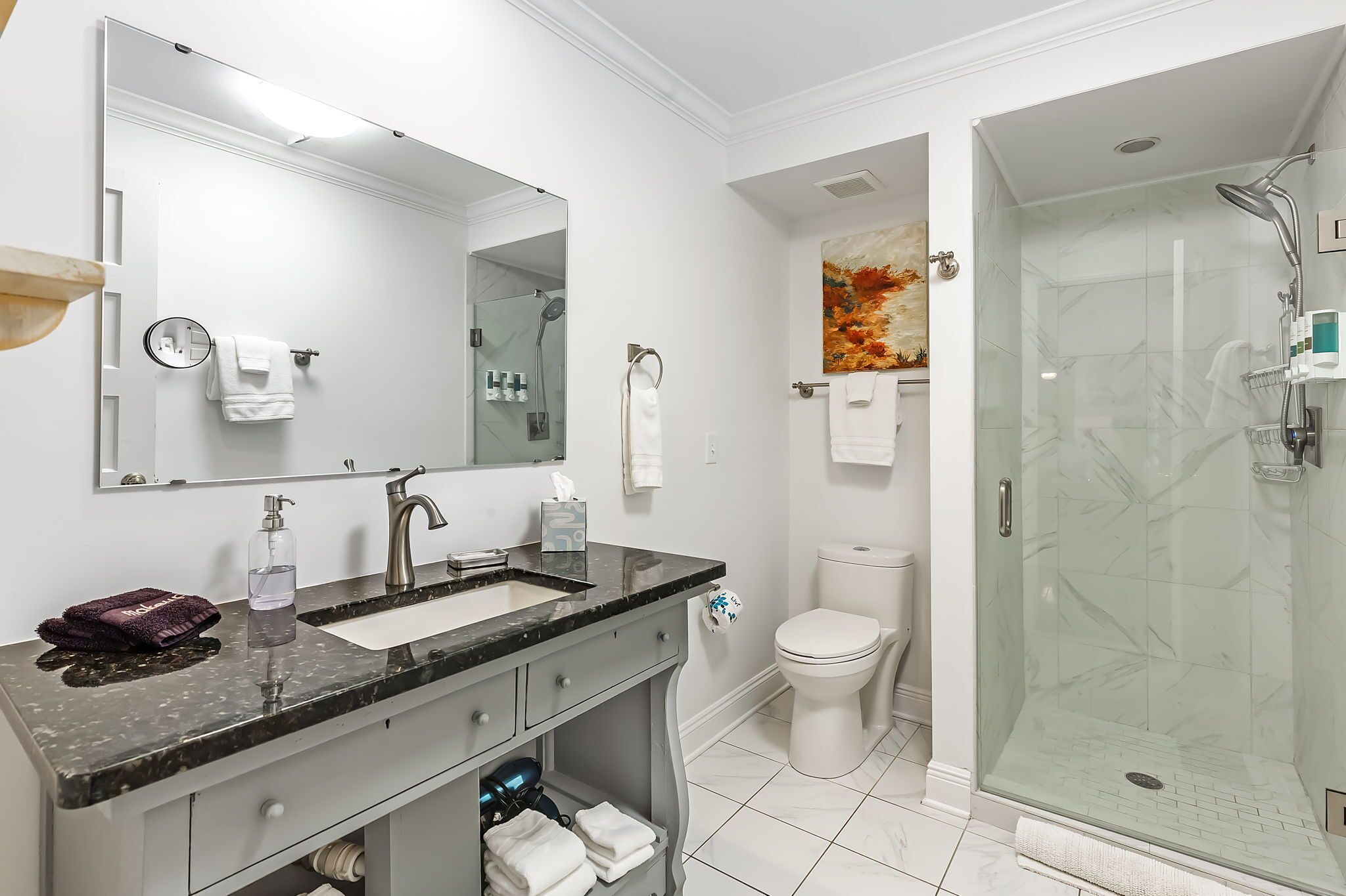 A modern bathroom with a large mirror, a sink, a toilet, and a glass-enclosed shower.