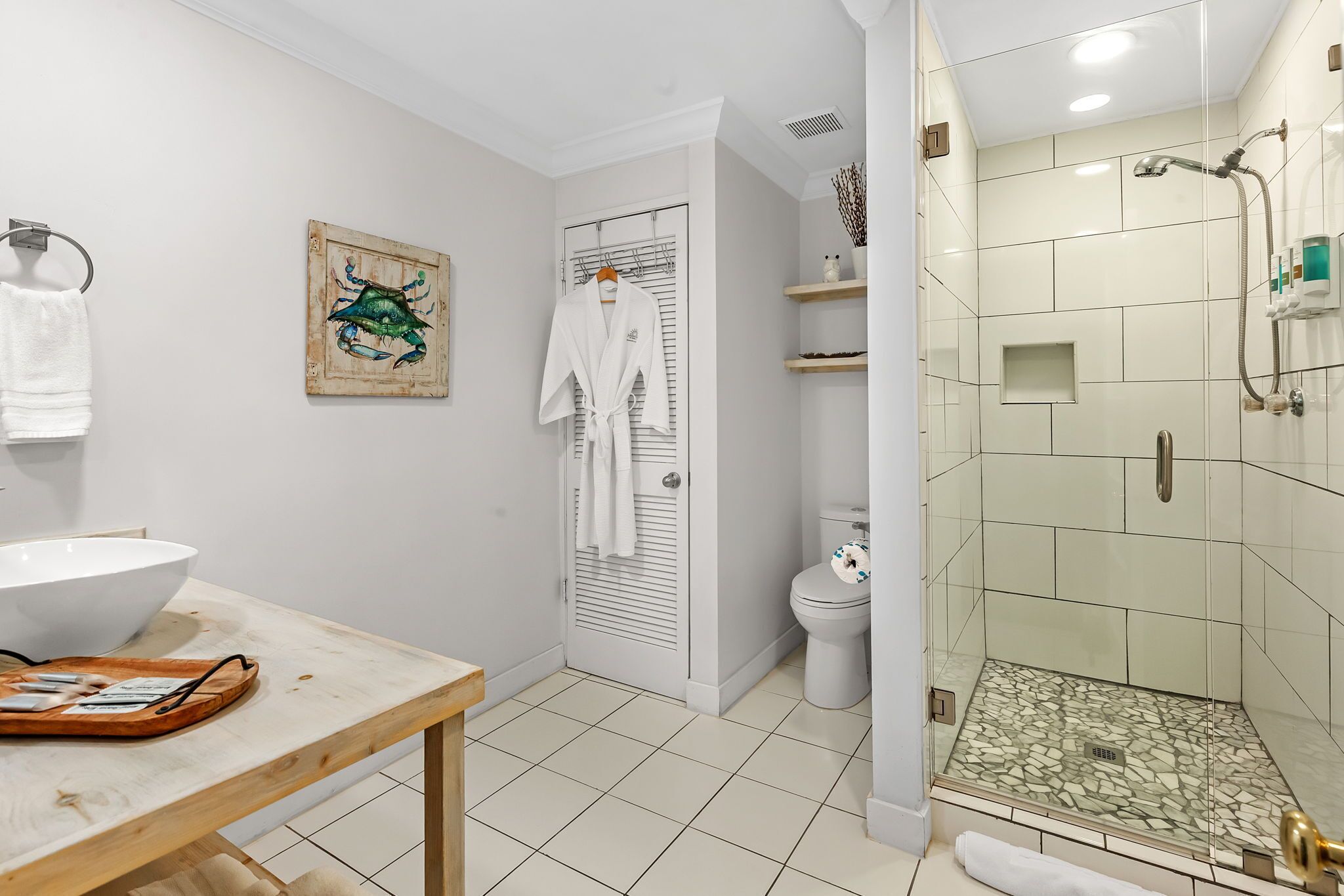 A modern bathroom with a glass-enclosed shower, a white sink, and a wooden table with toiletries.