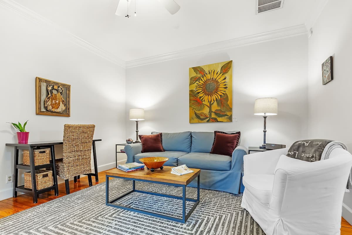Un salon avec un canapé bleu, une table basse, un fauteuil blanc et un tableau représentant un tournesol.