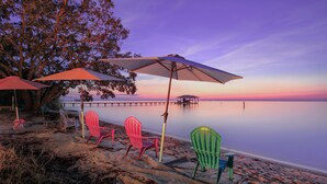 A beach with colorful chairs and umbrellas, a pier in the background, and calm water. - Jubilee Suites Boutique B&B (Fairhope)