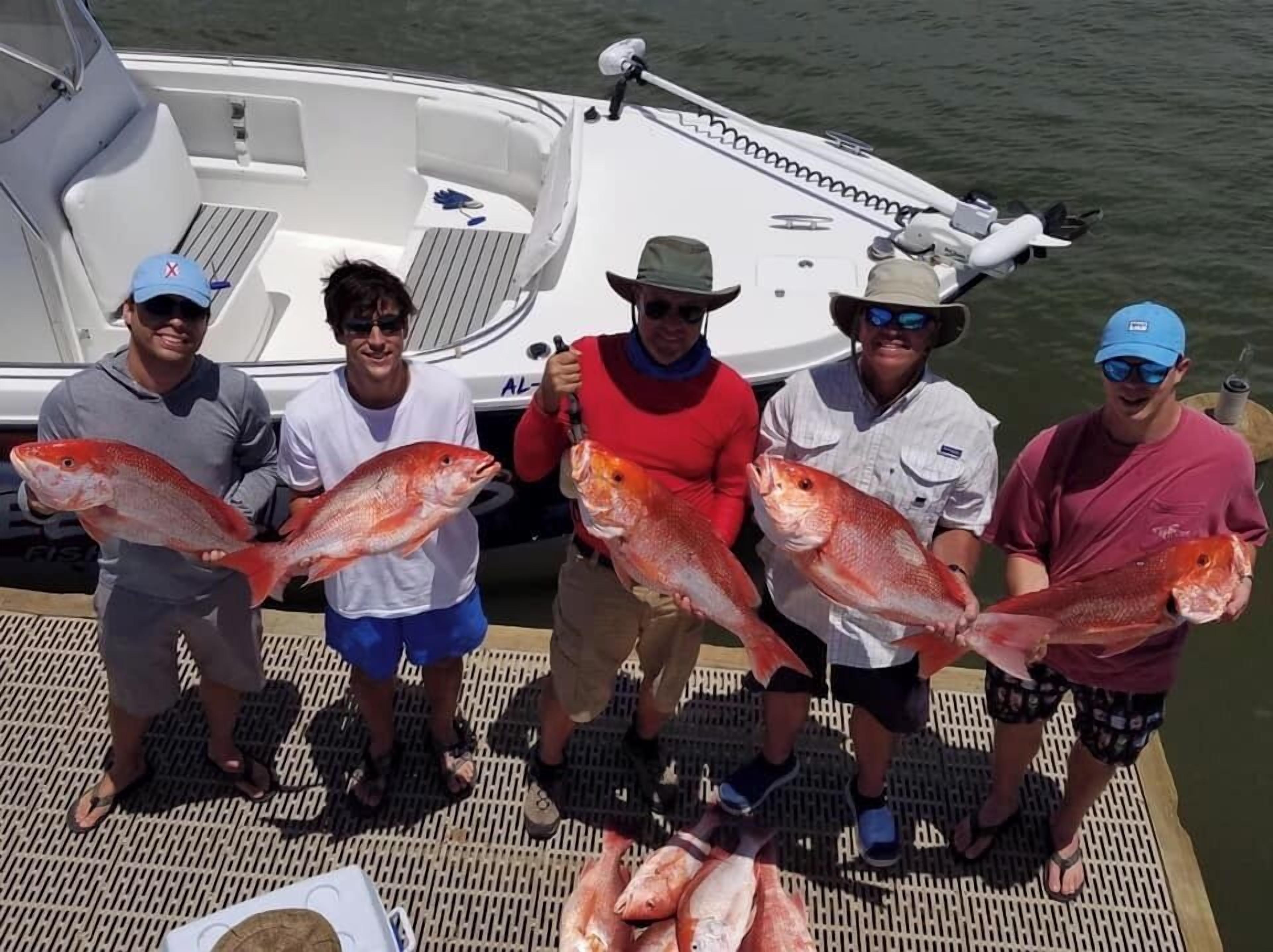 A group of people on a boat holding large fish, with a boat docked in the background.