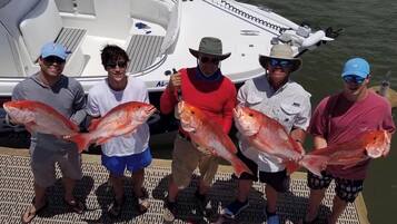A group of people on a boat holding large fish, with a boat docked in the background.