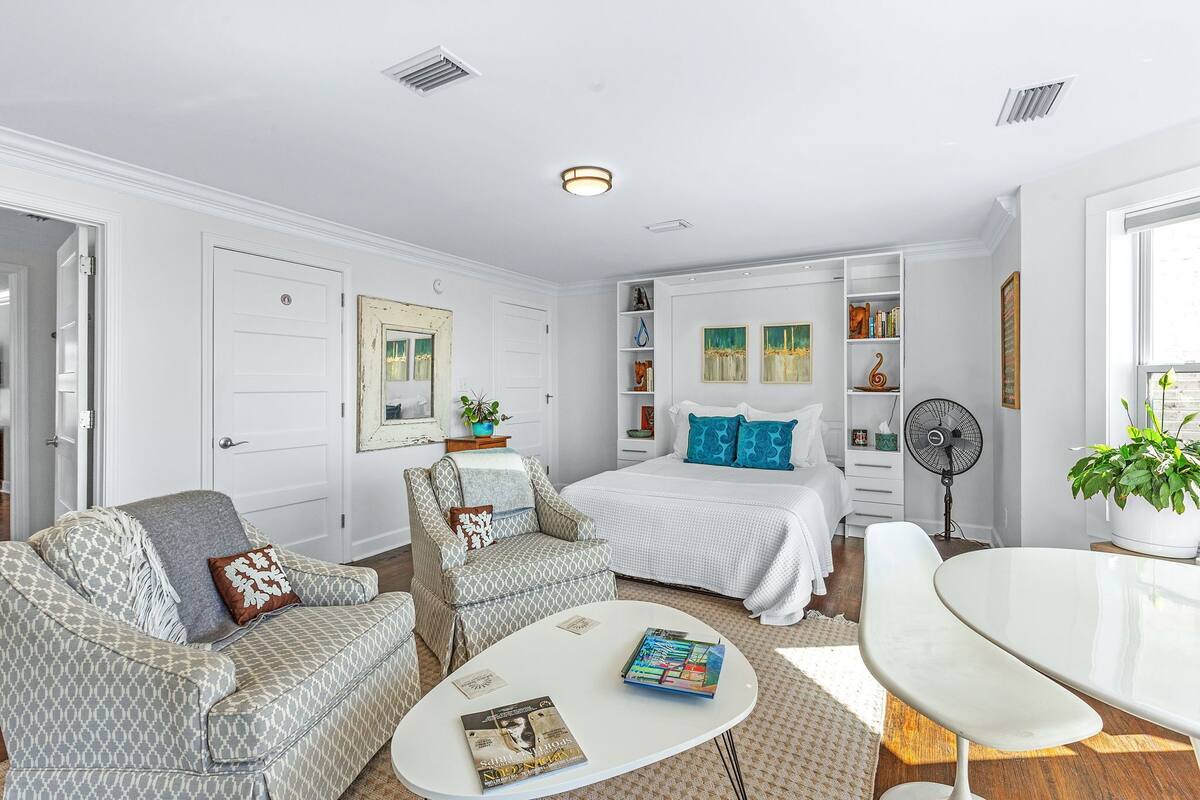 Une chambre à coucher moderne avec un lit, deux fauteuils, une table basse blanche et une table de chevet avec une lampe.