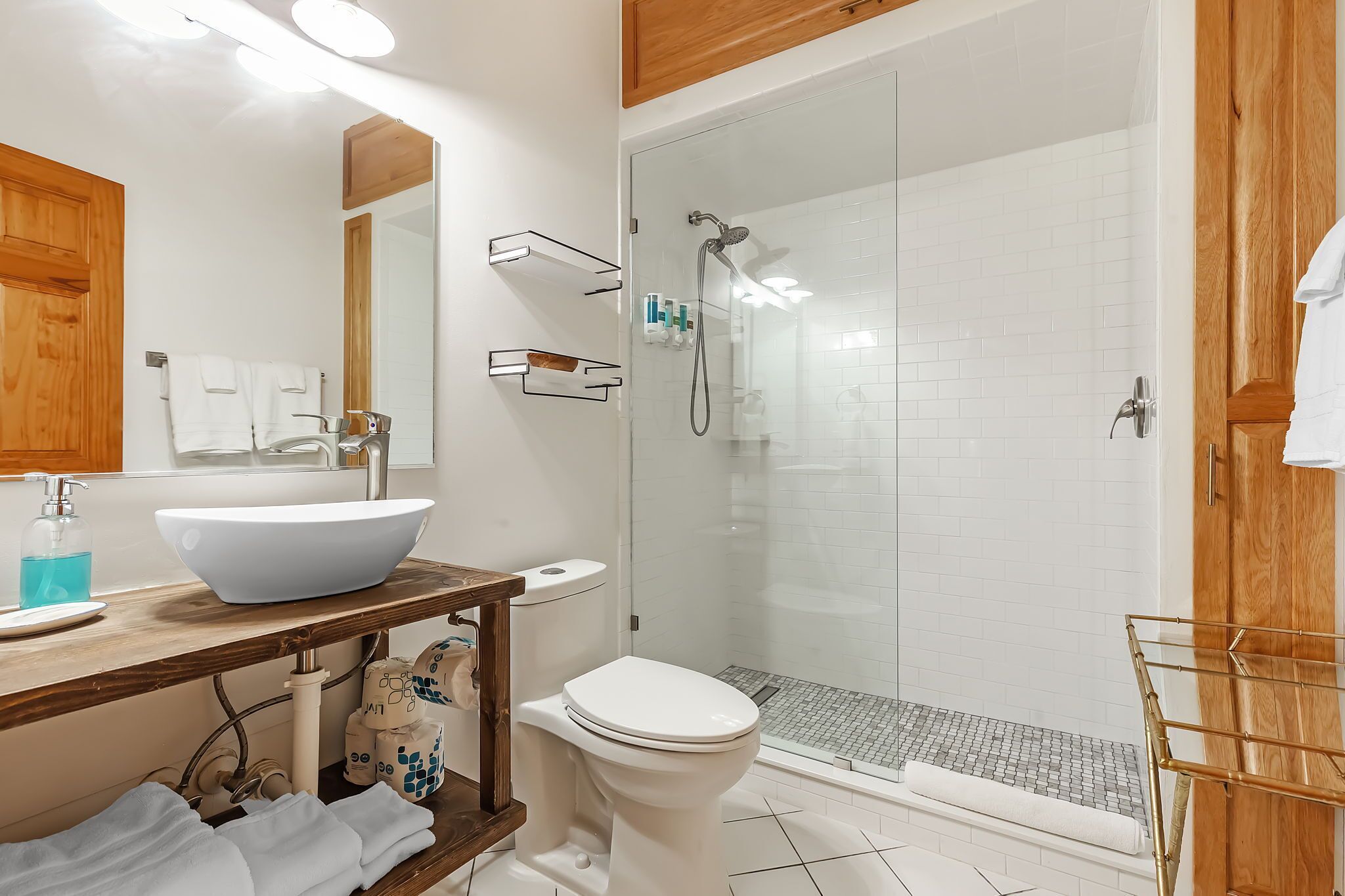 Un baño con lavamanos blanco, inodoro, ducha con cerramiento de vidrio y muebles de madera.