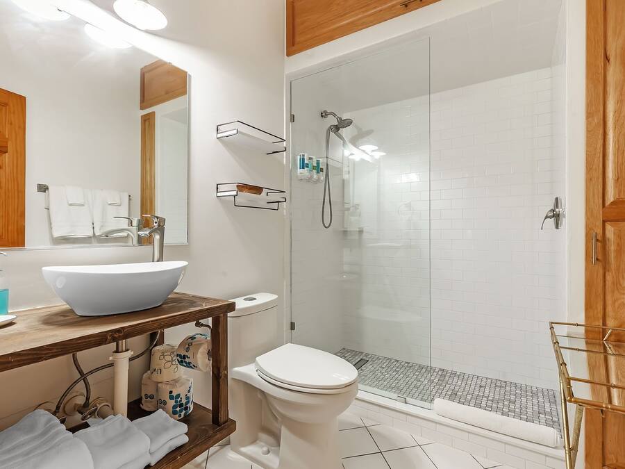 Un baño con lavamanos blanco, inodoro, ducha con cerramiento de vidrio y muebles de madera.