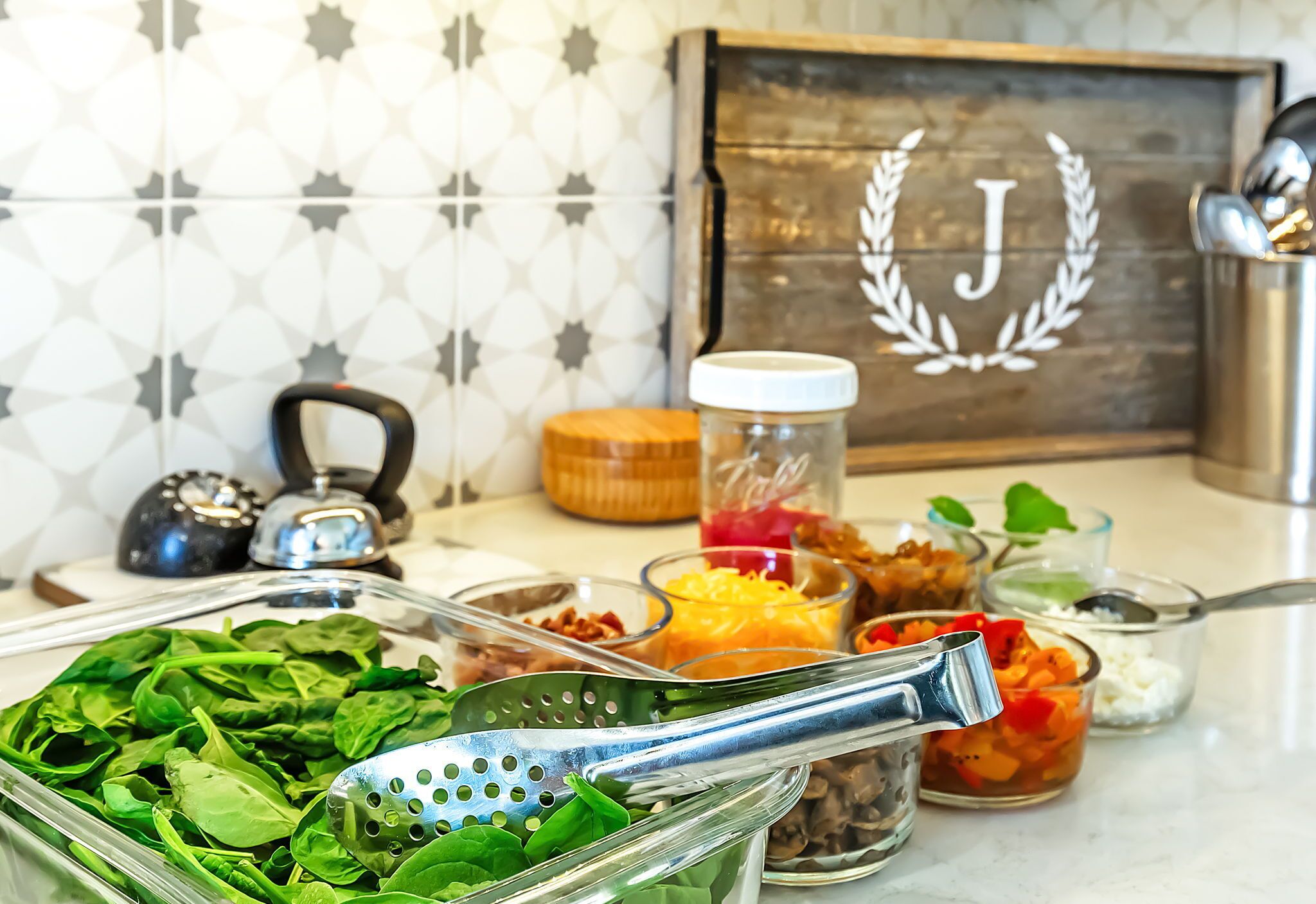 A kitchen counter with various food items and kitchenware, including a colander, jars, and a kettle.